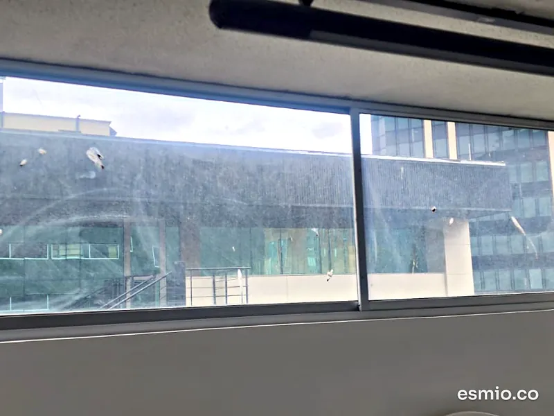 Antes: ventanal de oficina en Bogotá con el vidrio manchado de polvo, marcas y residuos secos, frente a un edificio de vidrio