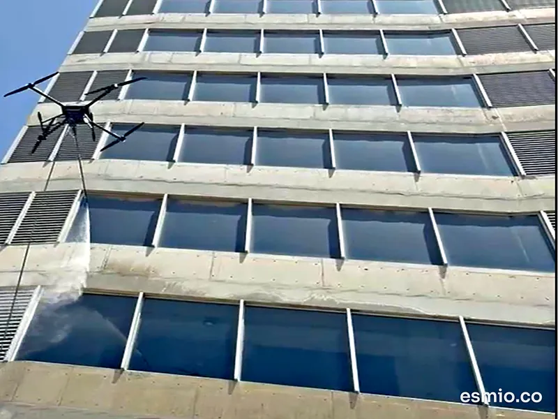 Dron de limpieza lavando con agua la fachada de concreto y vidrio de un edificio de varios pisos