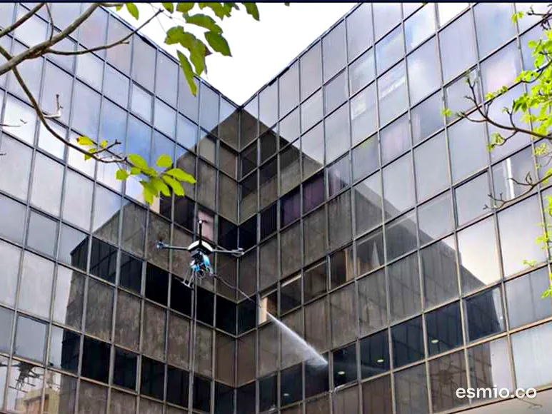 Dron lavando desde el aire la fachada de vidrio de un edificio de oficinas, visto desde la plazoleta