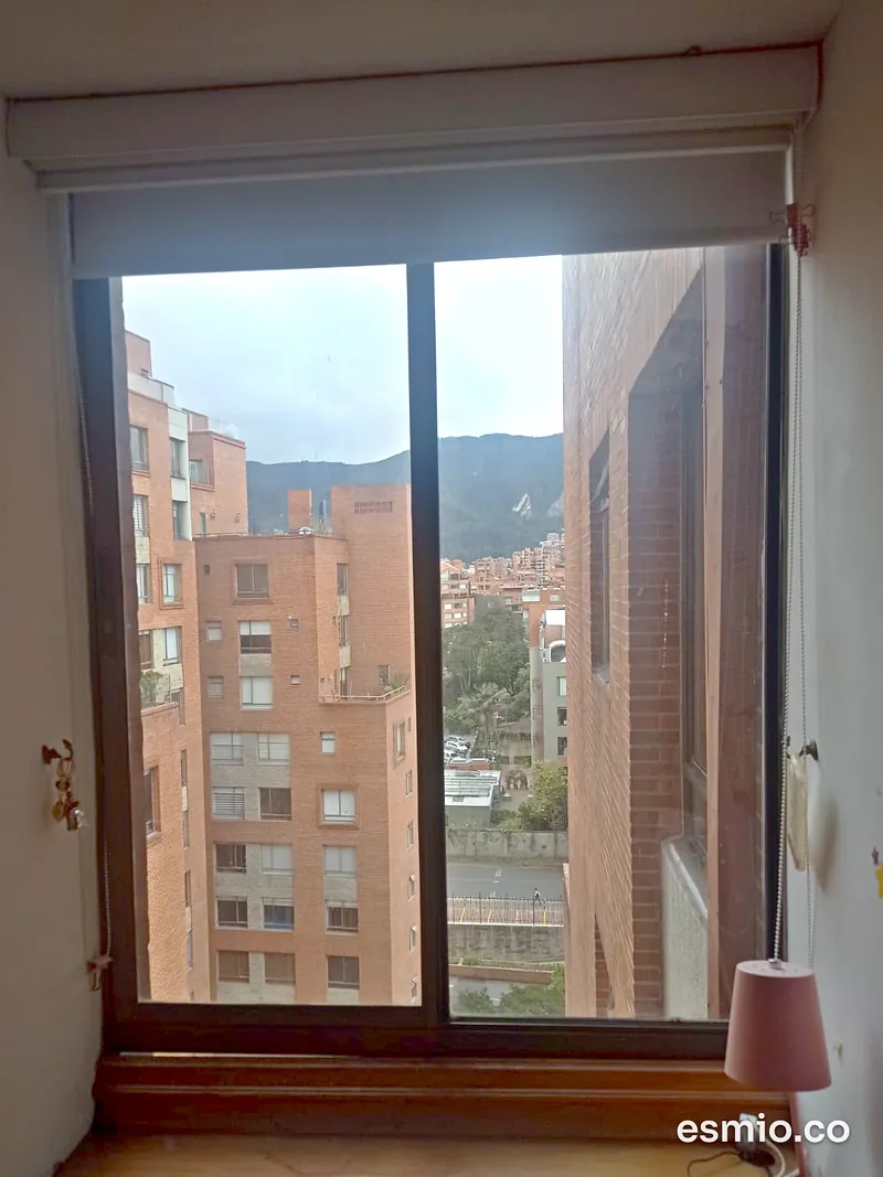 Ventana alta de apartamento con vidrio limpio y vista a edificios de ladrillo y a los cerros